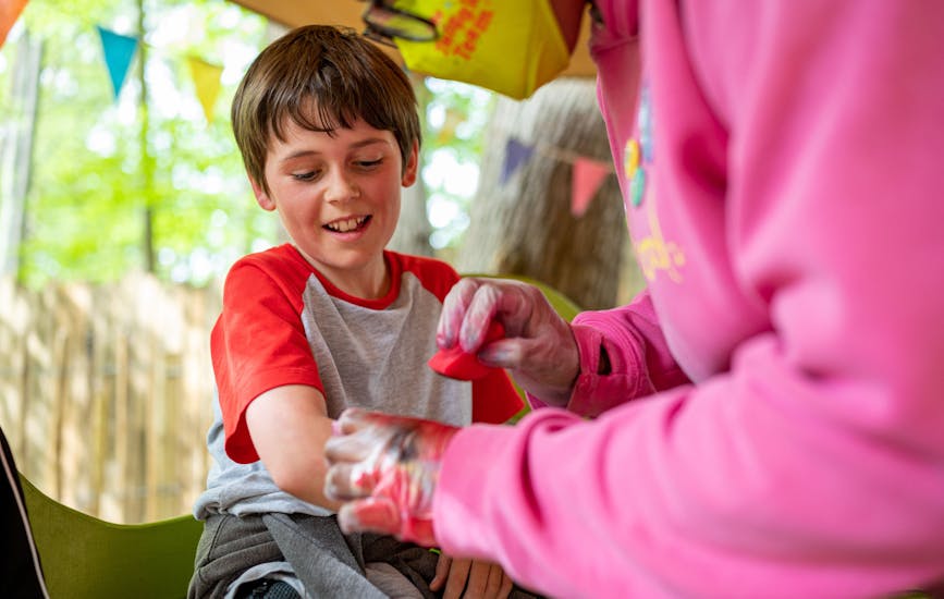 A smiling child has their arm painted at BeWILDerwood