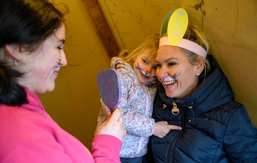A mother and child smile into a handheld mirror at their Easter bunny face paint.