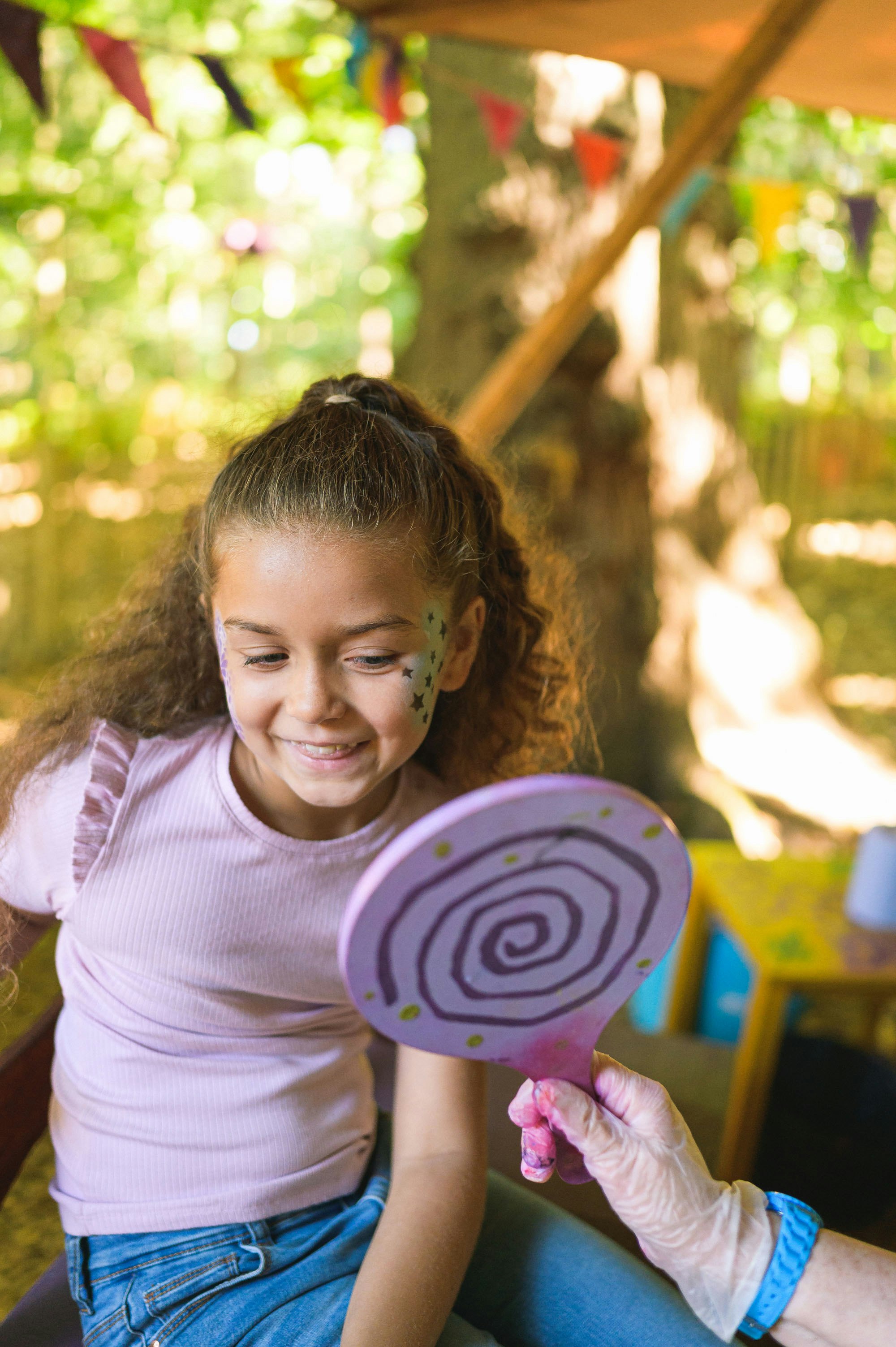 A girl smiles into a handheld mirror at her star face paint