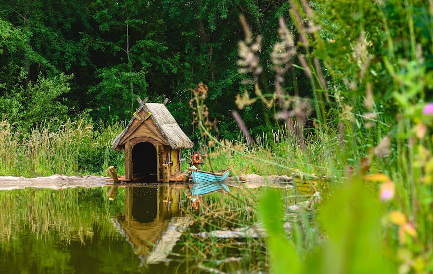 A wooden hut and a boat by the water of the Loopy Lakes in BeWILDerwood Cheshire