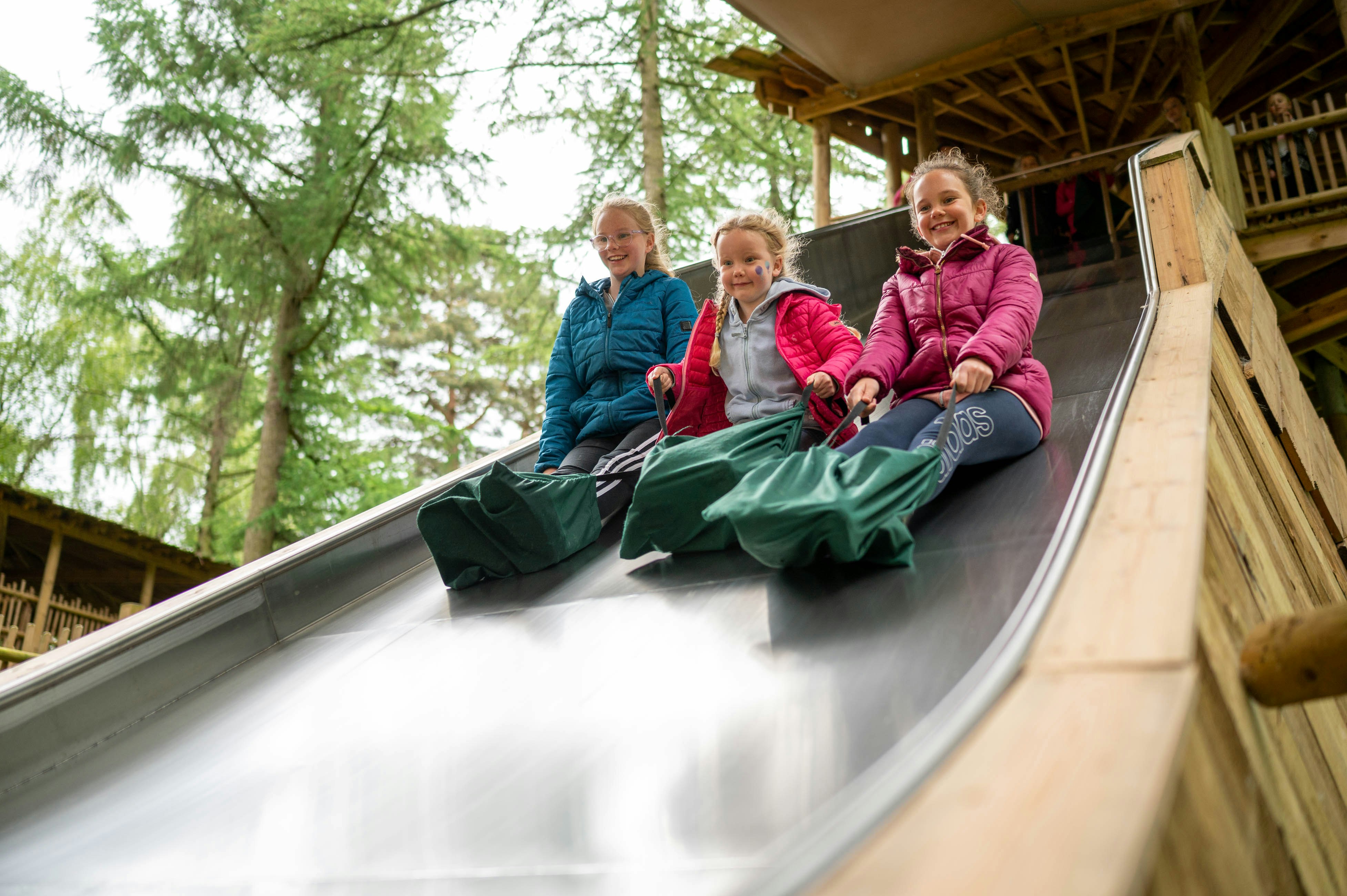 Three children use a wide slide at BeWILDerwood
