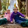 Two children in Easter bunny face paint and headbands smile as they slide down the Slippery Slopes at BeWILDerwood