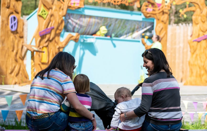 Two mothers and their children watch a story at the Storytelling Stage in BeWILDerwood Cheshire