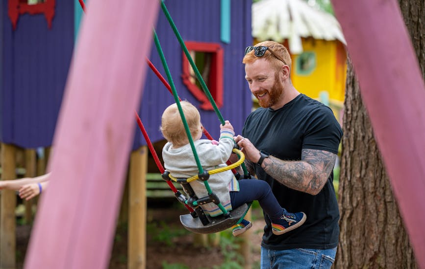 A father pushes their child in a swing at Toddlewood on the Hill