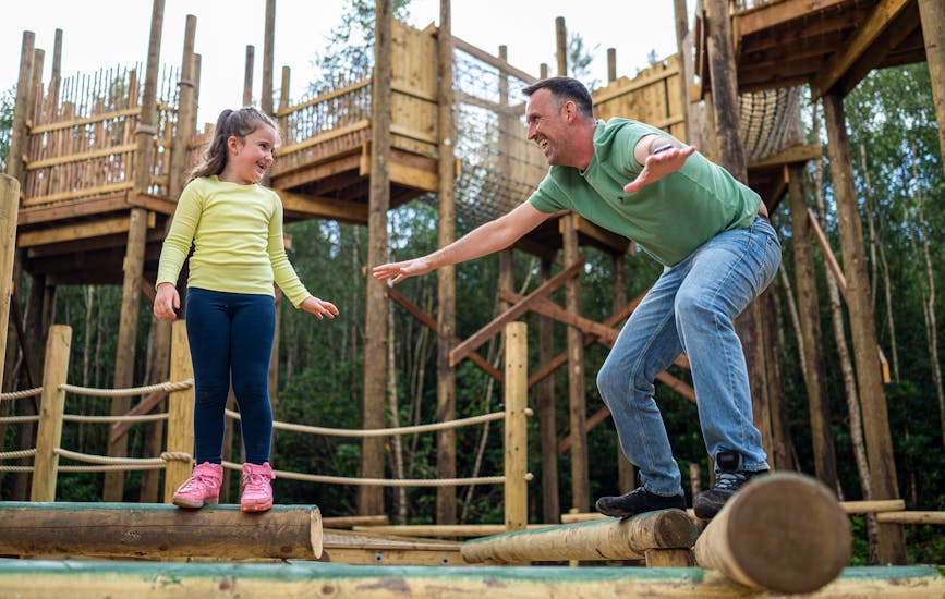 A parent and child play on wooden walk beams on The Towering Treetop Tangles