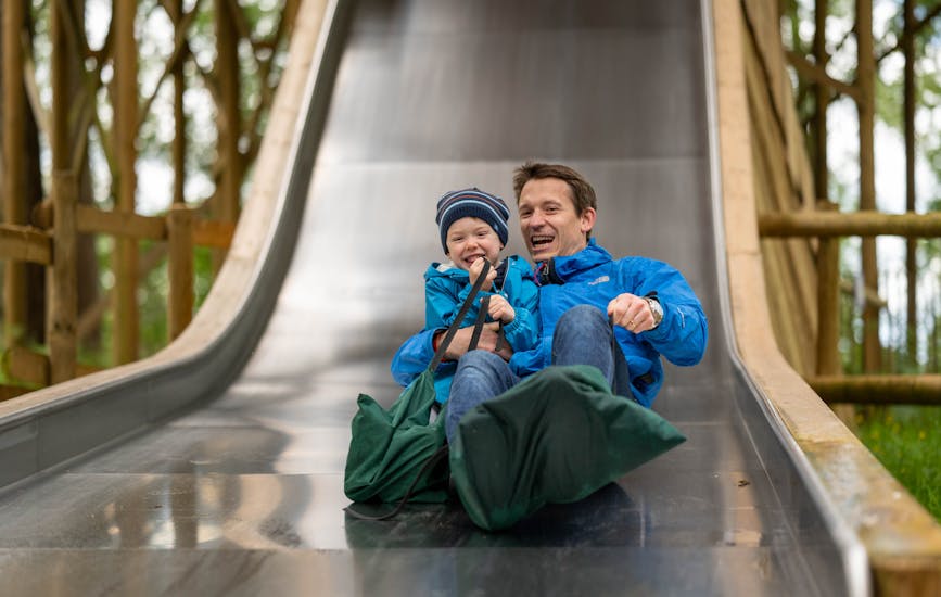 A father and child play together on a large slide at BeWILDerwood