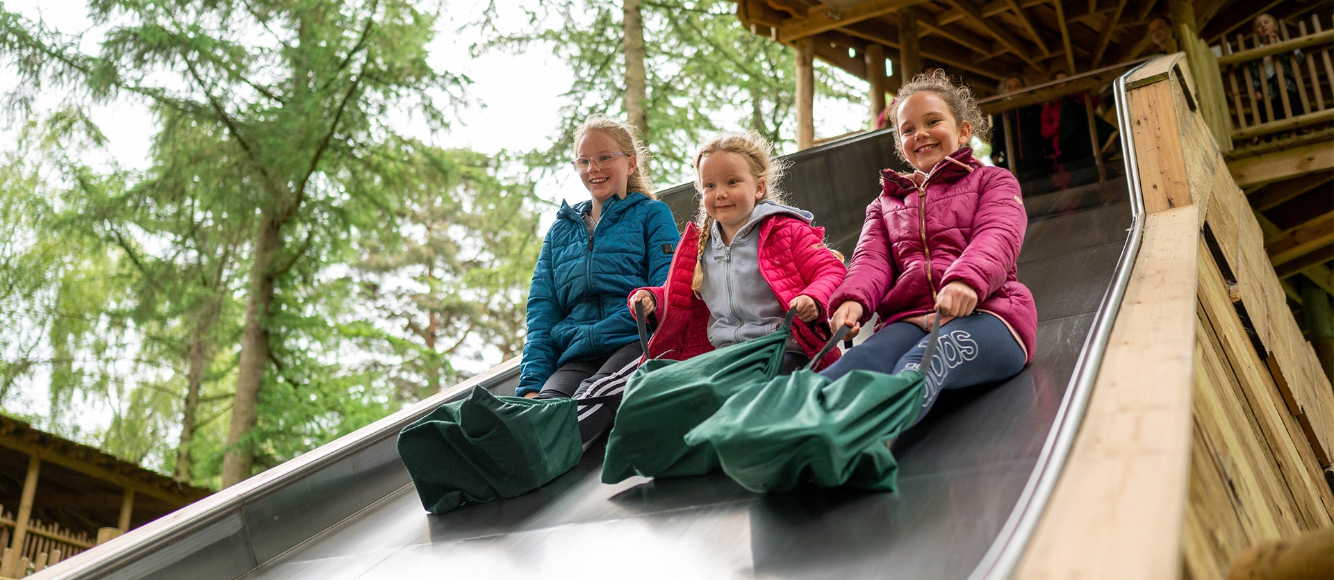 Three children play on the slippery slopes at BeWILDerwood