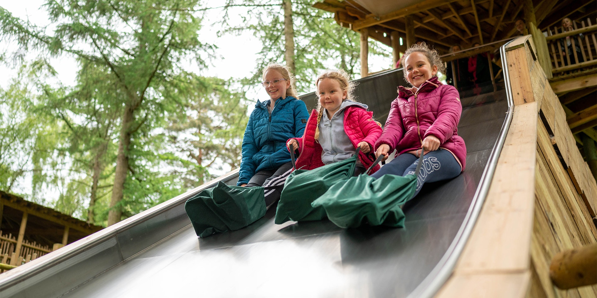 Three children slide down a big slide at BeWILDerwood
